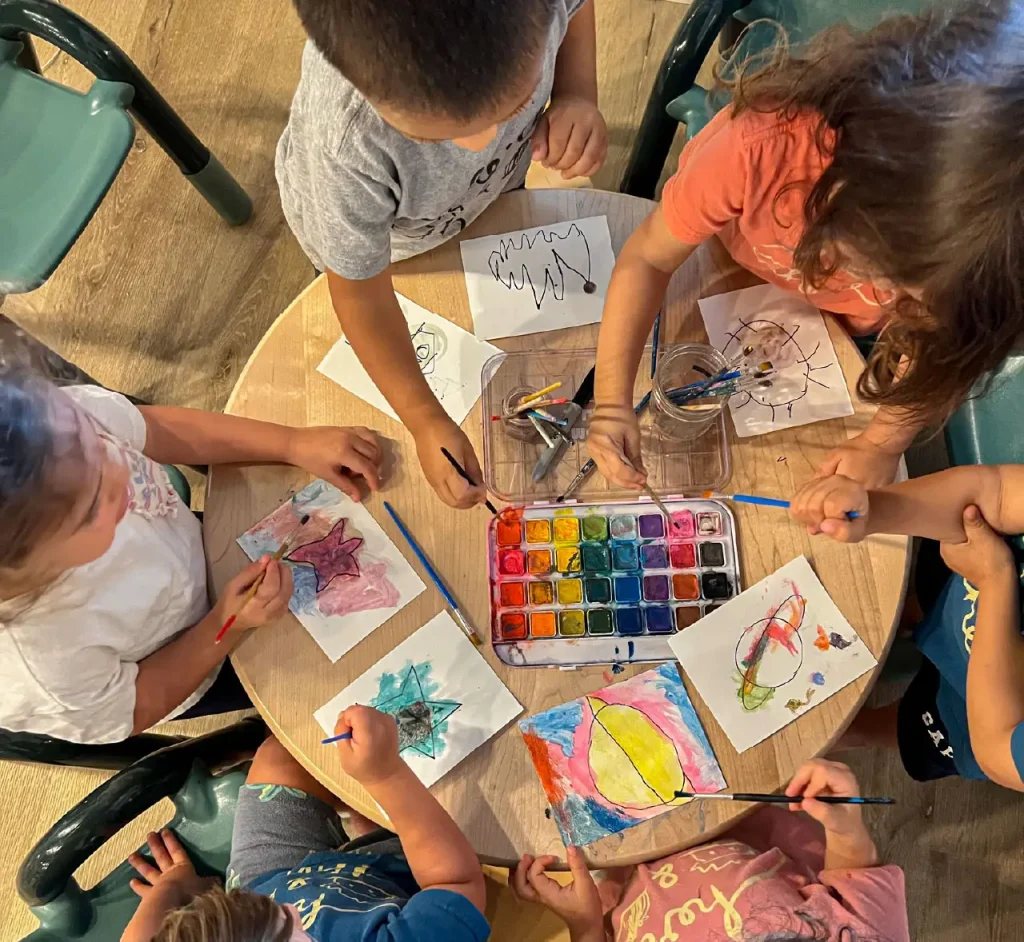 Children painting with watercolors in a screen-free classroom at Here & There Preschool